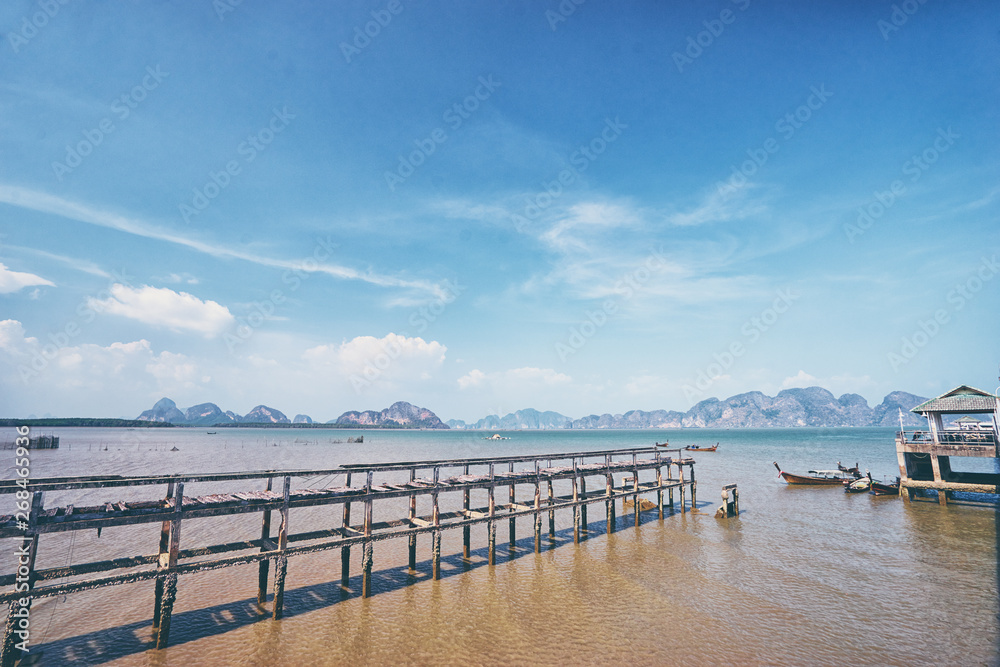 Beautiful old pier on the sea shore. Traveling by Thailand. Landscape with sea lagoon, pier and traditional fishing longtail boats.