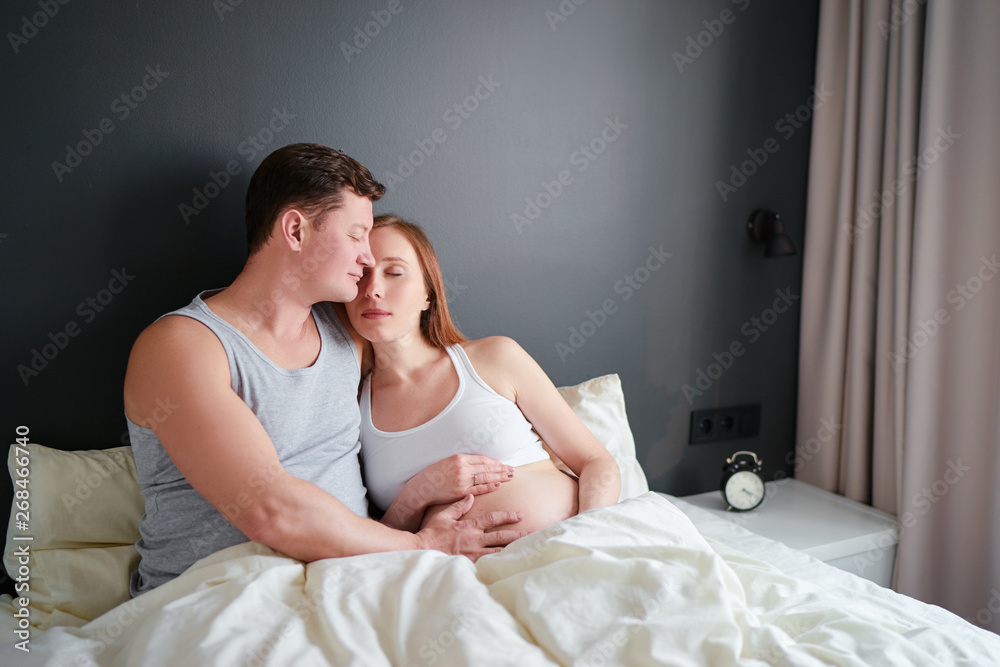 Happiness and tender. Husbang hugging his pregnant wife in bed.