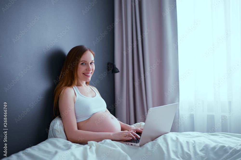 Technology, pregnancy and work. Pregnant woman using laptop computer sitting on bed at home. Technology, pregnancy and work. Pregnant woman using laptop computer sitting on bed at home.
