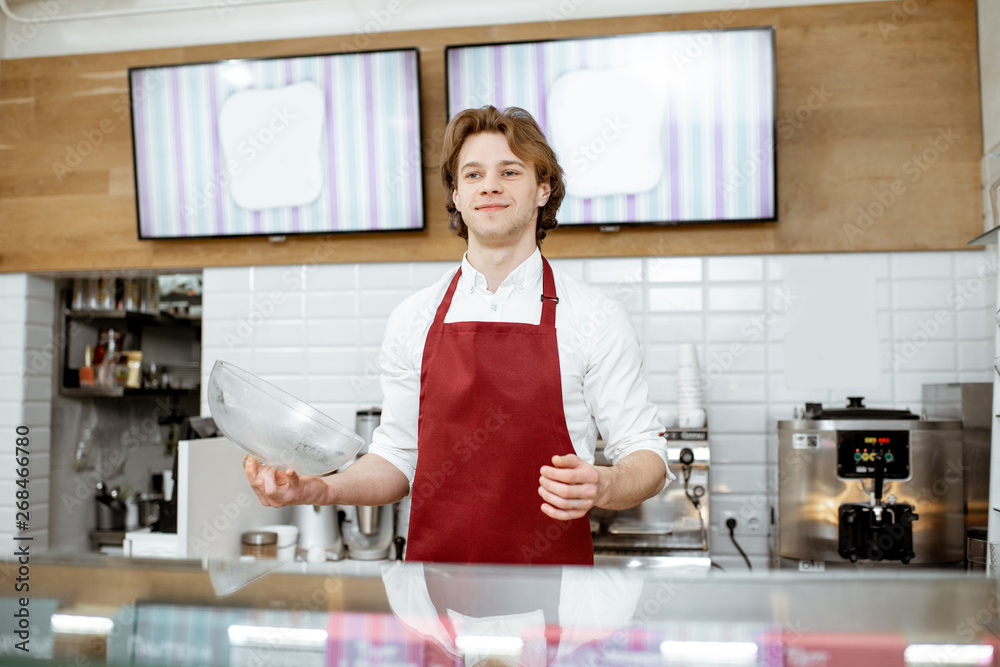 Portrait of a handsome salesman in red apron standing at the showcase of the modern pastry shop Portrait of a handsome salesman in red apron standing at the showcase of the modern pastry shop