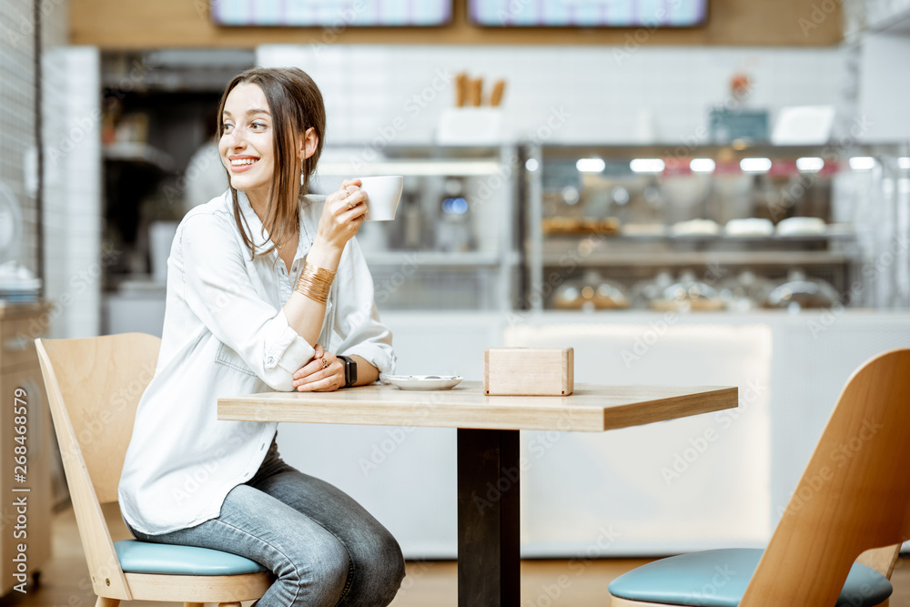 Young smiling woman drinking coffee while sitting in the modern pastry shop Young smiling woman drinking coffee while sitting in the modern pastry shop