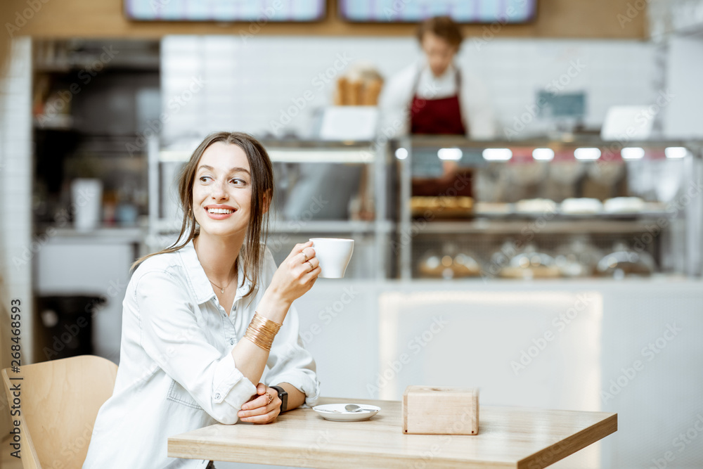Young smiling woman drinking coffee while sitting in the modern pastry ...