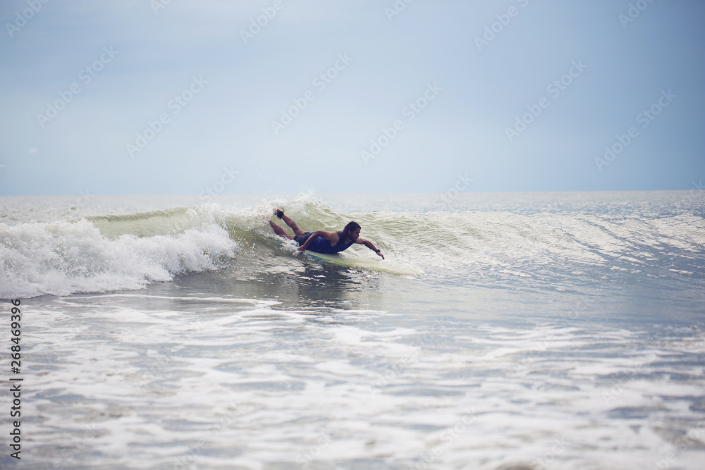 Naklejka premium Mixed race Surfer paddling with longboard on small wave