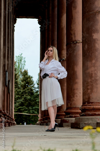 Fashion look's woman. Young woman modern portrait. Young woman dressed in white skirt and shirt posing near the old looking soviet union's architectural building with large pillars and bas-reliefs.