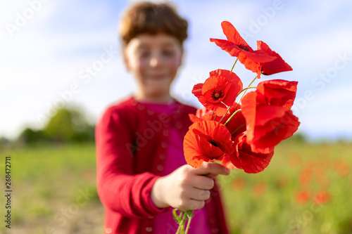 Bambina che offre dei fiori papaveri rossi su uno sfondo di campagna e cielo azzurro photo