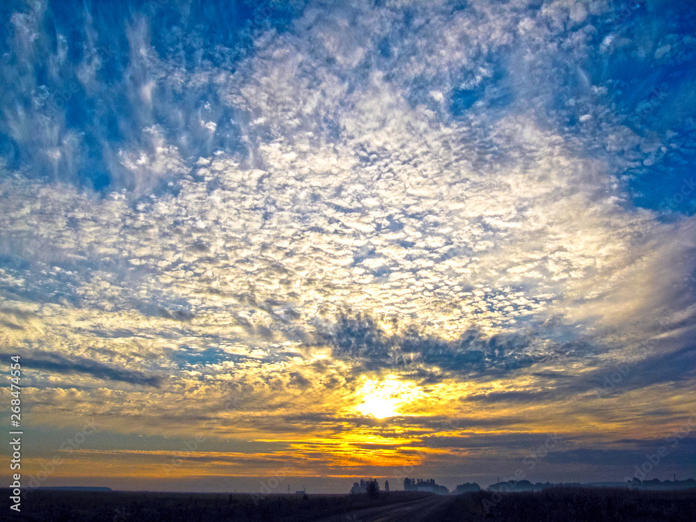 Autumn sunrise with fog. The sun's rays of the morning sun break through the clouds against the blue sky.