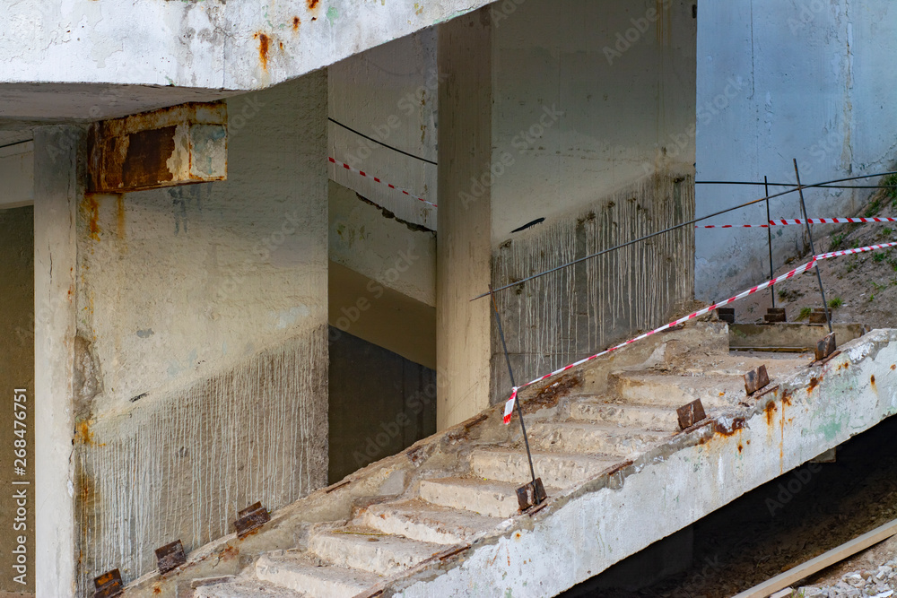 The edge of the concrete stairs leading to the bridge with a broken railing fenced off with a warning tape