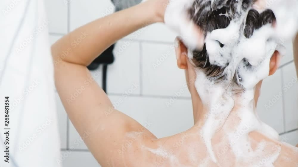 Rear view of a young beautiful woman washing her hair with soap shampoo. Concept of personal care and hygiene