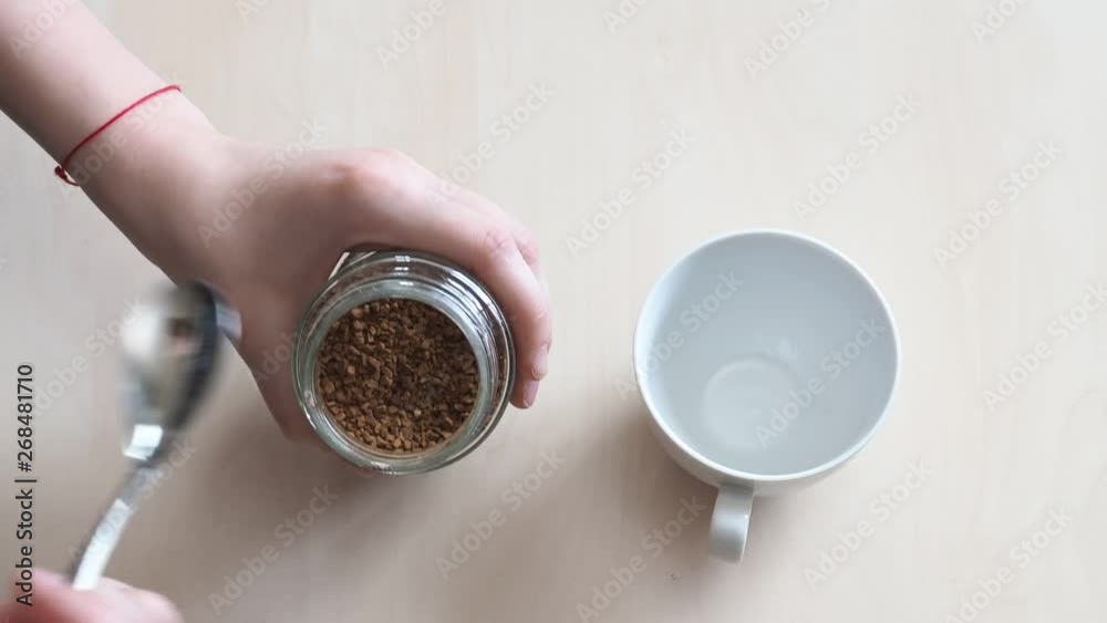 top view of hand puts two spoonful of instant coffee in cup top view of hand puts two spoonful of instant coffee in cup
