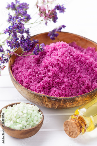 Sea salt in bowl, aroma oil in bottles, Wellness and flowers on grey textured background and flowers on vintage wooden background. Selective focus.