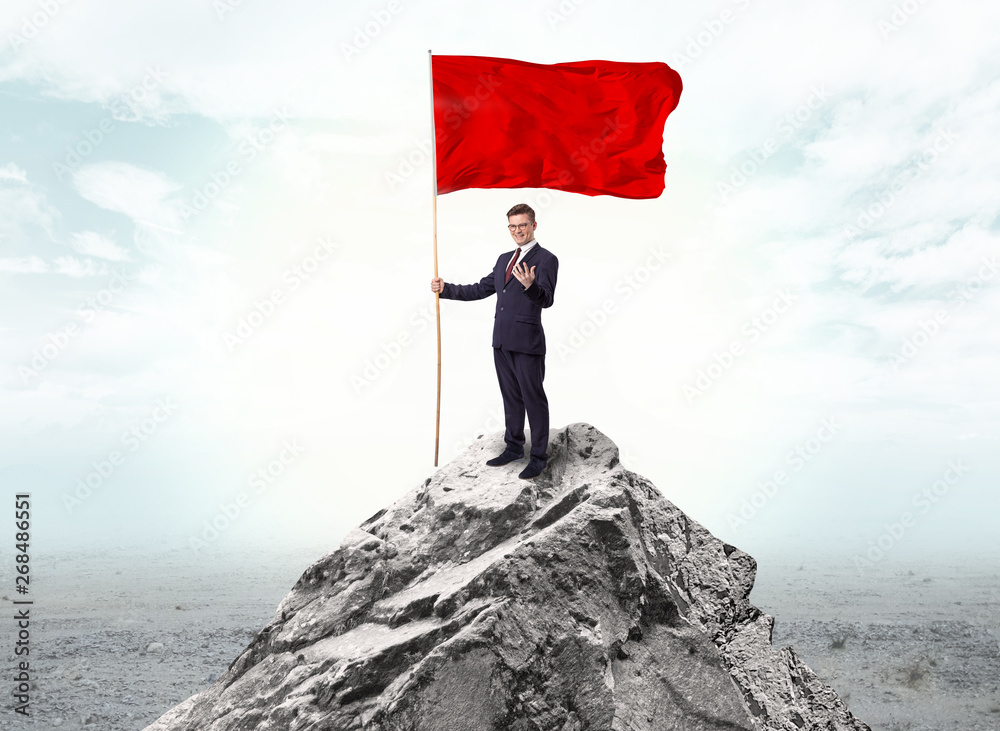 Handsome businessman on the top of the mountain with red flag
