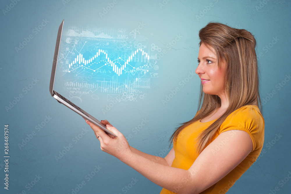 Woman holding laptop projecting financial information, diagrams and charts
Woman holding laptop projecting financial information, diagrams and charts