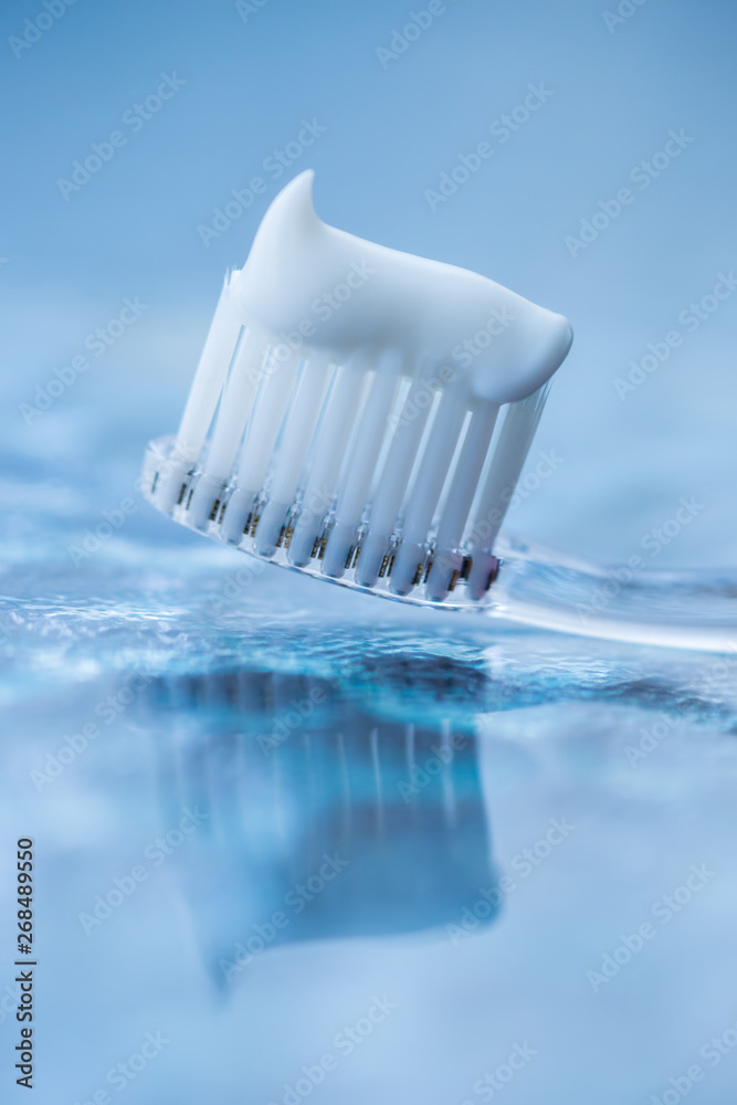 Transparent plastic toothbrush with white toothpaste on a blue white background with reflection on the glass.