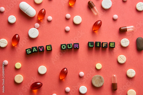 Multicolored title SAVE OUR LIFE from black cubes on the table with tablets on coral background