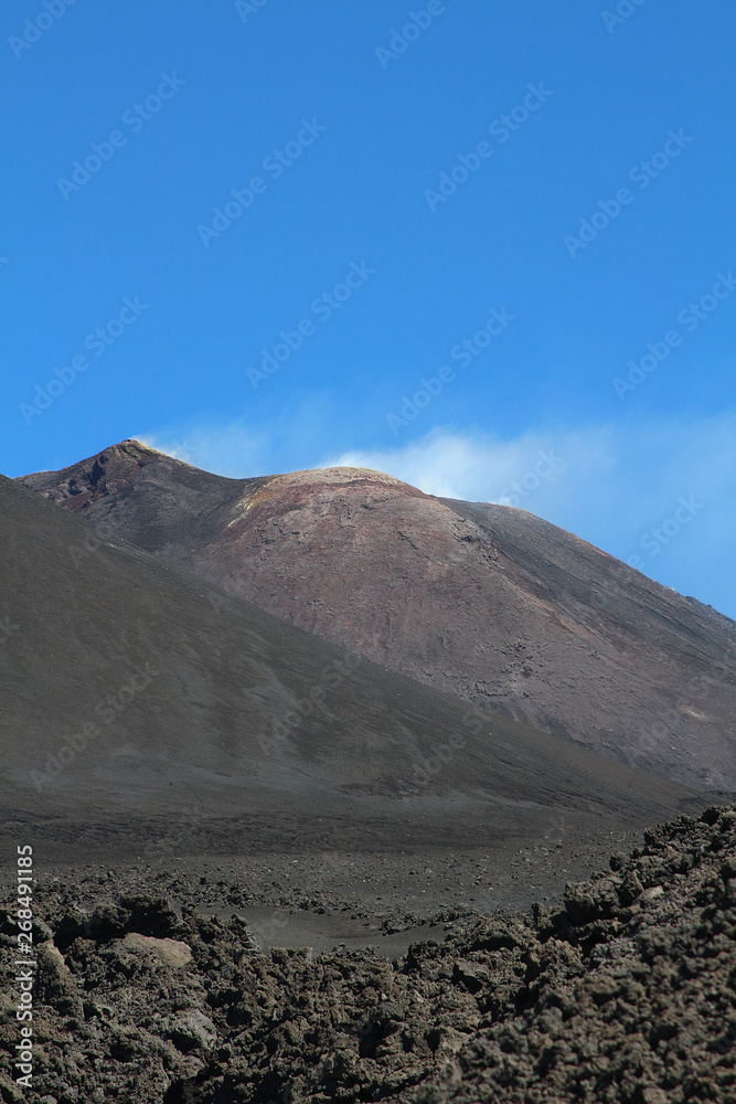 The black lava ash of smoking Volcano Etna against blue sky, Sicily, Italy
