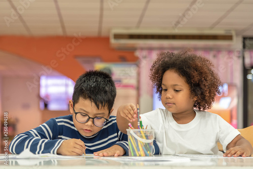 Little toddler girl and boy drawing together.  Asian boy and Mix African girl learn and play together in the pre-school class. Children enjoy hand writing. Friendship in class.