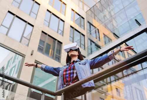 young woman with long hair in VR glasses on modern glass building background.