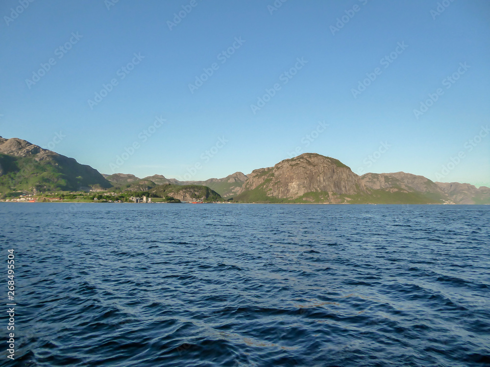 A wast fjord near Rogaland, Norway. Water of the fjord is slightly wavy. Bright sunbeams reflect in the water's surface. In the back tall mountains are shrouded in fog. A wast fjord near Rogaland, Norway. Water of the fjord is slightly wavy. Bright sunbeams reflect in the water's surface. In the back tall mountains are shrouded in fog.