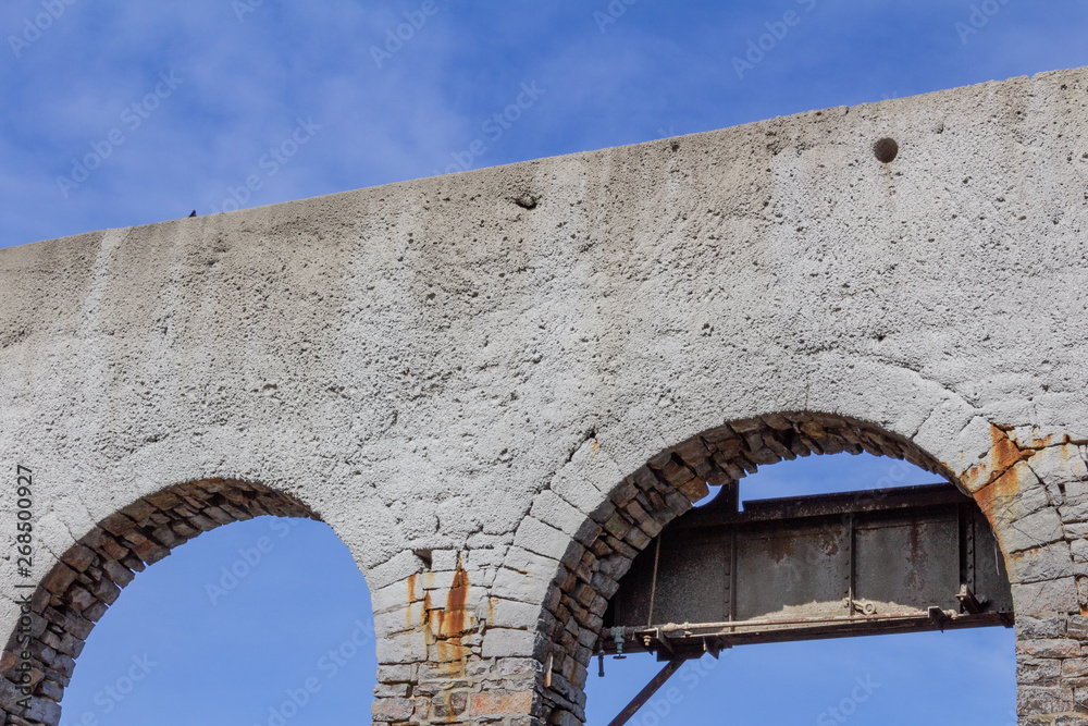 Open brick arches from an abandoned building, white with rusty metal against a blue sky, horizontal aspect