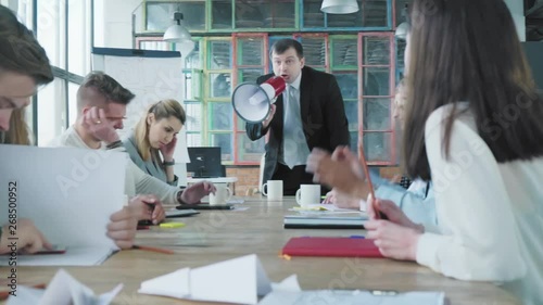 The manager in a business suit gets up from a chair, takes a megaphone in his hand, swears and shouts at the staff. The business team has a bad mood. Office life. Creative interior. Coworking
