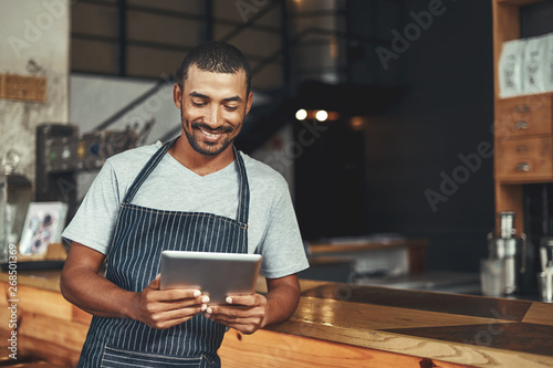 Smiling male cafe owner looking at digital tablet