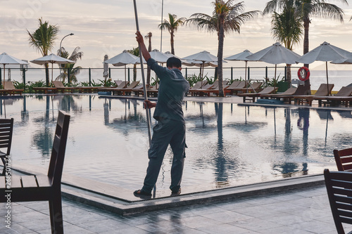A cleaner in overalls cleans the pool using special cleaning equipment. Service hotel territory