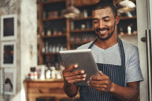 Successful barista cafe owner looking at digital tablet