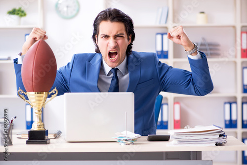 Young handsome businessman with rugby ball in the office