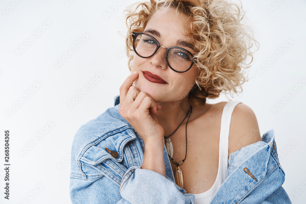 Close-up shot of romantic and self-assured modern girl with blond hairstyle and glasses smiling flirty and tender holding fingers on jawling gazing cute at camera over white background Close-up shot of romantic and self-assured modern girl with blond hairstyle and glasses smiling flirty and tender holding fingers on jawling gazing cute at camera over white background