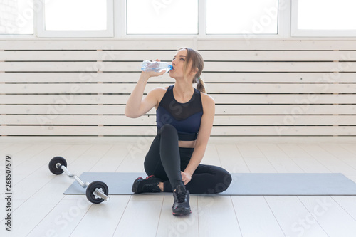 People, sport and fitness concept - young woman sitting with bottle of water on gym mat © satura_