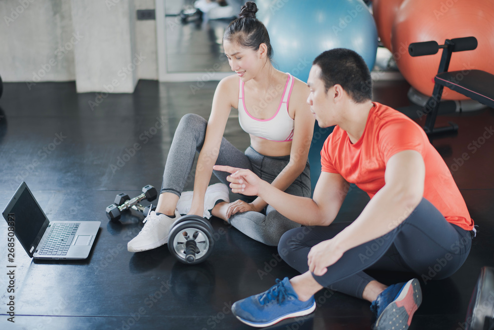 Obraz premium Sport women and men fitness trainer are discussing. Young Asian female talking with coach during workout with at gym. Female coach explaining with laptop computer.