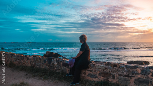 Senior woman sitting on wall during sunset in Galle Fort, Sri Lanka © CHAO