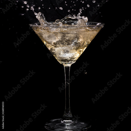 in a martini glass  vermouth ice falls  and splashes with drops on a black background