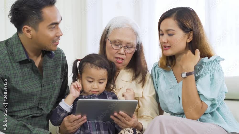 Happy little girl using a digital tablet with her parents and grandmother while sitting on the sofa at home. Shot in 4k resolution Happy little girl using a digital tablet with her parents and grandmother while sitting on the sofa at home. Shot in 4k resolution