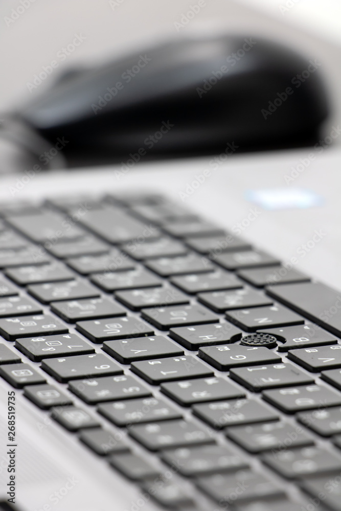 Close-up view of keyboard with mouse in blurred background on black table. Empty desktop with computer equipment in office.