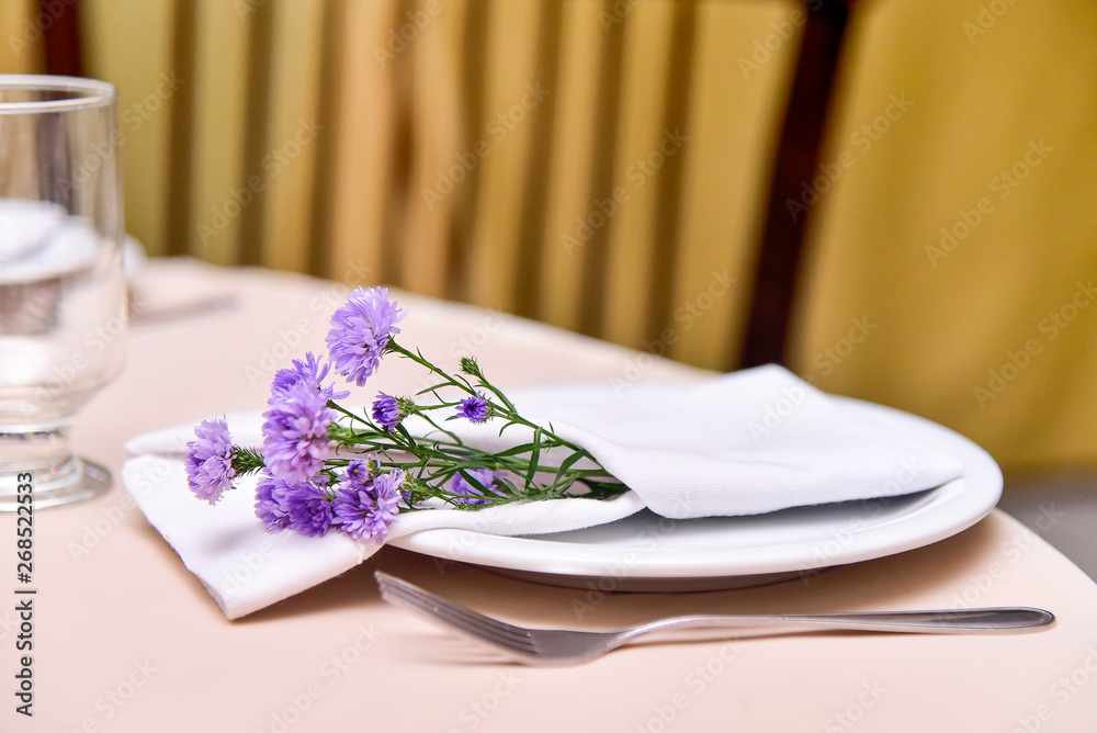 table setting with white plate and napkin with lilac flower. table setting with white plate and napkin with lilac flower.