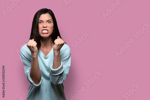 Woman with extreme rage, clinched fists and jaw, angry, emotional, and furious, isolated on pink background, copy space photo