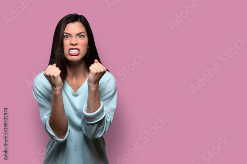 Woman with extreme rage, clinched fists and jaw, angry, emotional, and furious, isolated on pink background, copy space
