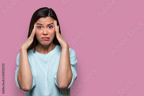 Isolated facial expression of a worried, concerned, fearful, regretful woman, expressing distress and inner conflict, pink background photo
