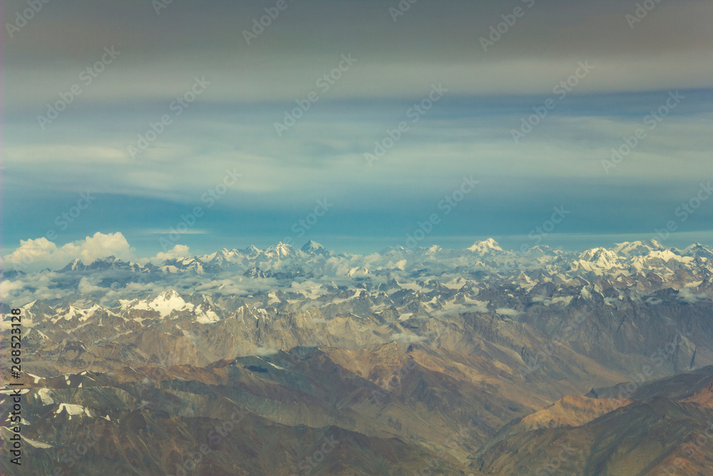 Himalayan desert yellow mountain valley with snowy peaks under a blue sky with white and dark clouds aerial view