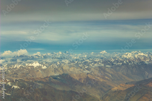 Himalayan desert yellow mountain valley with snowy peaks under a blue sky with white and dark clouds aerial view