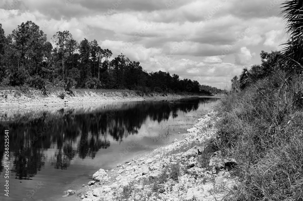 Beautiful scenic view of the great cypress basin canal in Golden Gate area of Naples Florida, showing clear clean water, cloudy sky and trees on the banks, shot with zone system. Beautiful scenic view of the great cypress basin canal in Golden Gate area of Naples Florida, showing clear clean water, cloudy sky and trees on the banks, shot with zone system.