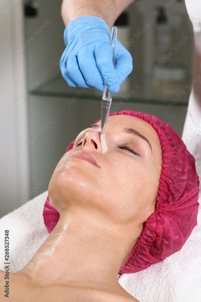 A cosmetologist puts a remedy on the face for the patient to nourish, moisturize and rejuvenate the skin. Cosmetic procedure in the clinic. Close-up of the patient's face. Beautician office