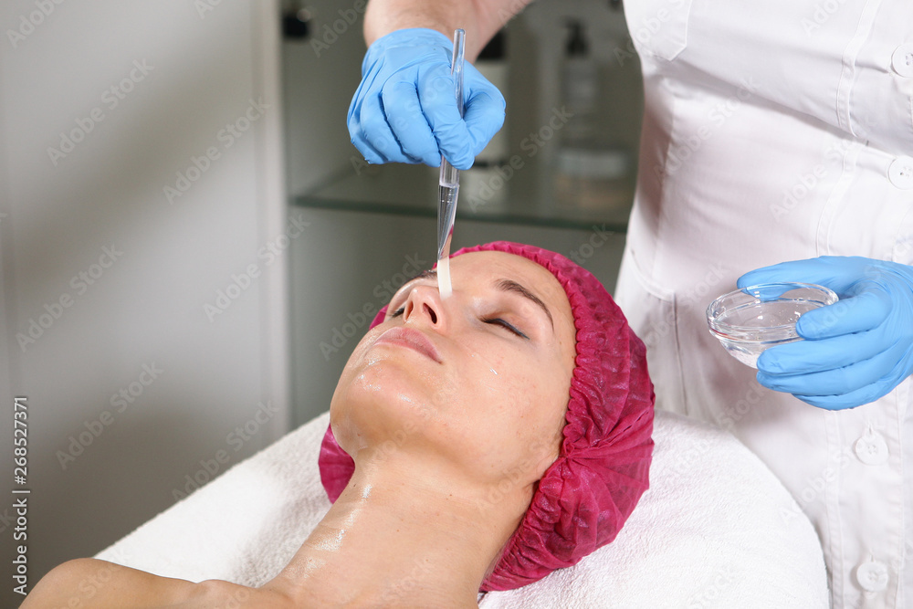 Naklejka premium A cosmetologist puts a remedy on the face for the patient to nourish, moisturize and rejuvenate the skin. Cosmetic procedure in the clinic. Close-up of the patient's face. Beautician office