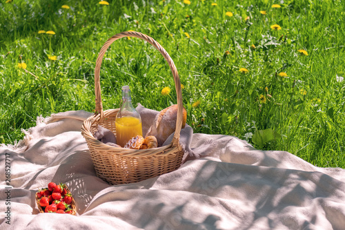 a fragment of a picnic on the green grass. Basket with bread and a bottle and strawberries in the basket