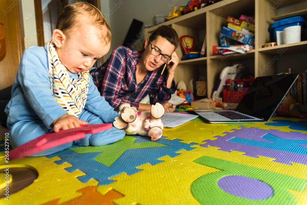 Fototapeta premium Mother working on her computer while taking care of her baby at home, multitasking woman, concept of work feminism and upbringing.