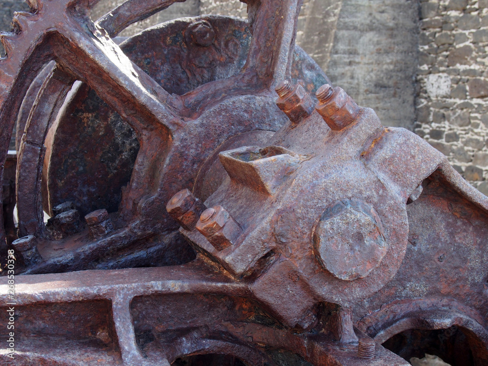 close up of an axle and broken spoked wheel on old rusted abandoned industrial machinery against a stone wall