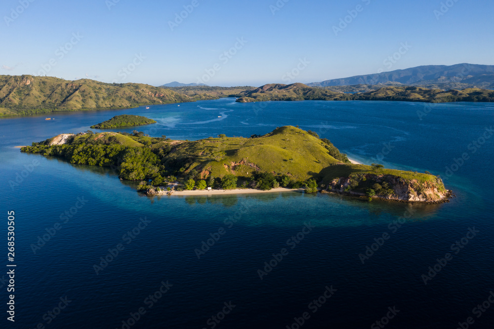 Obraz premium Seen from a bird's eye view, an idyllic island is surrounded by a healthy coral reef in Komodo National Park, Indonesia. This tropical area is known for its marine biodiversity as well as its dragons.