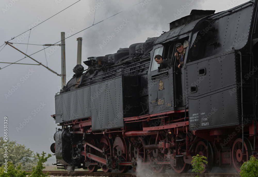 Obraz premium Historic steam locomotive with passenger wagons speeding on railroad tracks curve and blowing heavy white smoke near Sofia