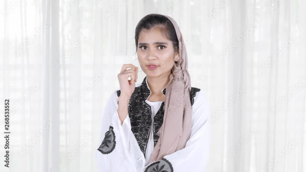 Beautiful young Asian muslim woman standing at home while thinking and looking at the camera. Shot in 4k resolution Beautiful young Asian muslim woman standing at home while thinking and looking at the camera. Shot in 4k resolution